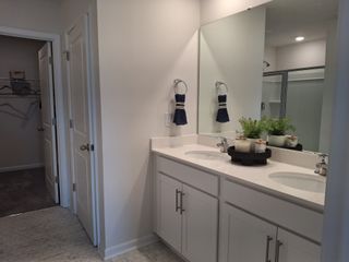 A modern bathroom with dual sinks, sleek white cabinetry, decorative plants, and chic hexagon-tiled flooring.