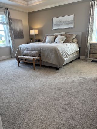 A bright bedroom boasts plush carpeting, natural light, and a stylish upholstered bed, creating a comfortable and inviting retreat.