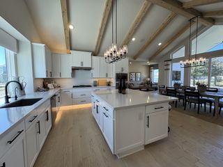 A spacious kitchen with vaulted ceilings, wooden beams, elegant pendant lights, and an open dining area.