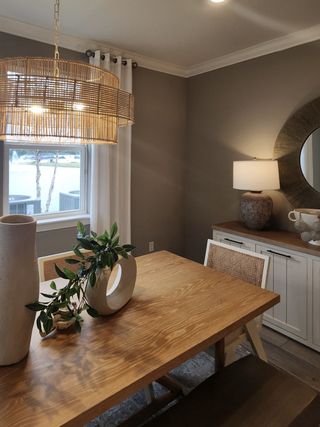 A beautifully designed dining area with a natural wood table, woven pendant light, and large windows that provide ample natural light and a scenic lake view.