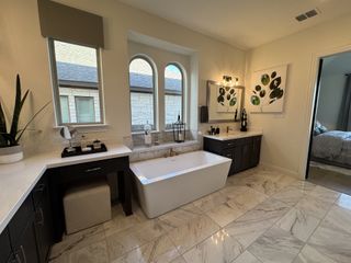 A luxurious bathroom featuring a sleek freestanding tub, elegant vanities, and artful decor with marble flooring.