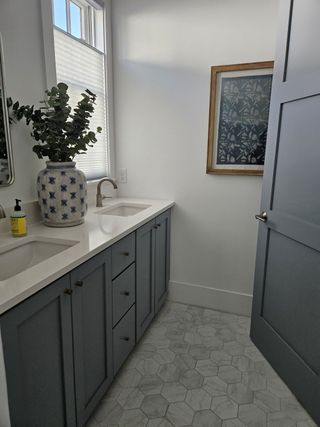 A stylish bathroom with a blue vanity, white countertops, and hexagonal tile flooring, accented with a framed artwork.