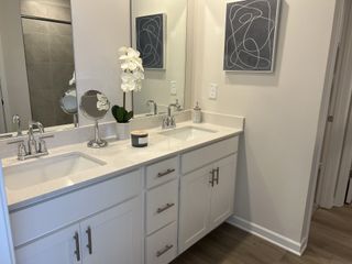 A contemporary bathroom with a double vanity, white cabinetry, quartz countertops, modern art, and a decorative orchid, creating a serene space.