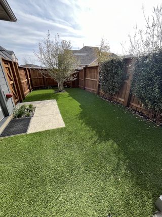 A cozy backyard with lush artificial grass, a small tree, and wooden fencing for privacy.