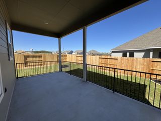 A charming covered patio with railing, overlooking a fenced backyard and neighboring houses under a clear blue sky.