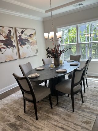 A chic dining area with a dark oval table, elegant gray chairs, abstract art, and large windows providing natural light.