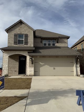 Street view A charming stone two-story home with shutters in South Brook by David Weekley Homes (Leander, TX).
