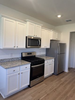 A modern kitchen with sleek white cabinets, granite countertops, stainless steel appliances, and stylish wood flooring.