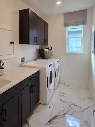 A functional laundry room with a white washer and dryer, dark cabinetry, and elegant marble-look flooring.