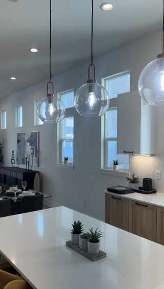 A modern kitchen features sleek pendant lights, white countertops, and minimalistic decor for an elegant ambiance.