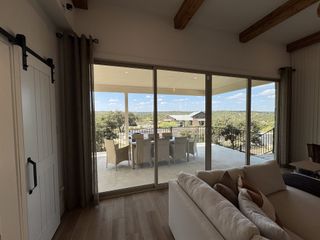 Model Home A living room with sliding glass doors opening to a covered patio with dining space, showcasing scenic outdoor views and natural light.