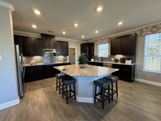 A modern kitchen with dark cabinetry, a granite island, and stylish chevron backsplash, complemented by sleek wood flooring.