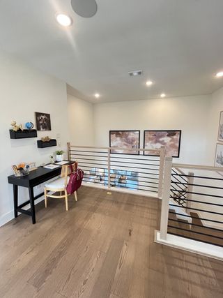 A cozy landing area with sleek wooden flooring, desk space, and modern railings overlooking the living room.