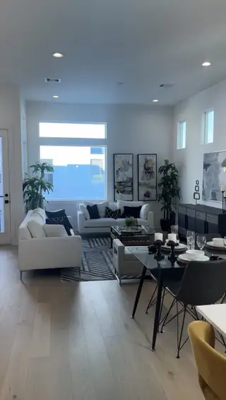 A modern living room with white sofas, abstract artwork, and chic decor, featuring large windows and a dining area.
