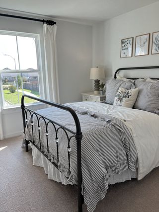 A cozy bedroom with a metal bed frame, striped bedding, and elegant decor. Bright natural light streams through the window.