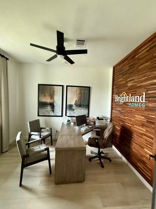 A modern office with a sleek wooden wall, minimalist desk, and cozy seating, accented by contemporary art and a ceiling fan.