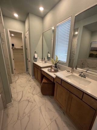 Model Home A spacious bathroom with dual vanities, warm wood cabinets, marble-patterned tile floors, and soft blue walls creates an elegant, relaxing space.