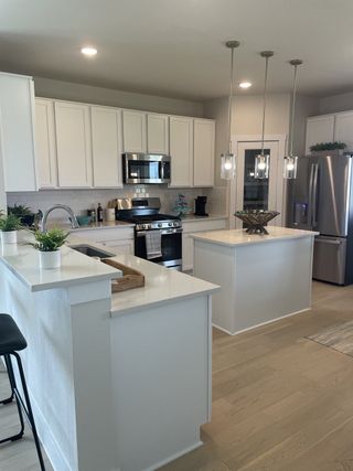 A modern kitchen featuring white cabinetry, stainless steel appliances, pendant lighting, and a spacious island.
