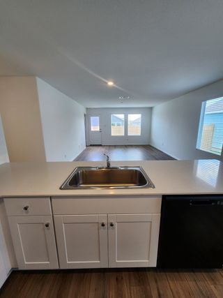 A spacious kitchen with sleek white cabinetry, a stainless-steel sink, and wood flooring, leading into a bright open living area.