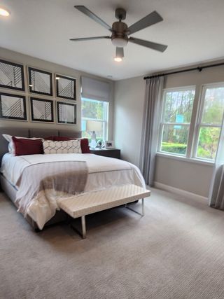 A cozy bedroom featuring a modern ceiling fan, plush carpeting, and elegant wall art, with a bench at the foot of the bed.