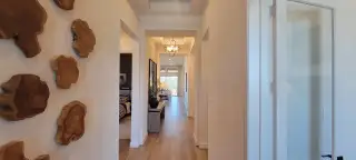 Model Home A bright hallway features wood accents, elegant lighting, and warm flooring, leading to a cozy living area.