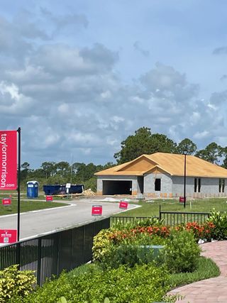 Street view A beautiful under-construction home in Veranda Oaks by Taylor Morrison in Port St. Lucie, FL, amidst lush greenery.
