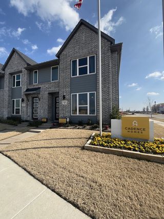 A stunning townhome exterior with brick and siding accents, lush landscaping, and a welcoming entrance in Solterra Texas by Cadence Homes (Mesquite, TX).