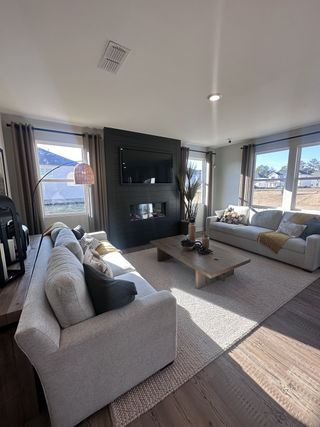 A cozy living room with light gray sofas, a dark accent wall, modern fireplace, and large windows for natural light.