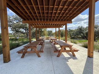 A charming outdoor picnic area in Wolf Ranch by Perry Homes, with rustic wooden tables and a pergola, ideal for community gatherings in Georgetown, TX.