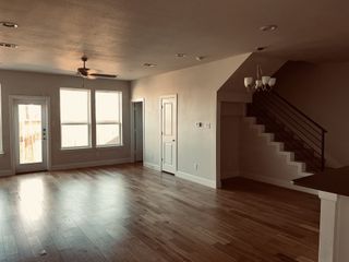 An open-concept living area with wooden floors, large windows, and a modern staircase beneath elegant lighting fixtures.