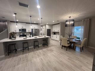 A modern kitchen and dining area with sleek cabinetry, pendant lighting, an island with bar stools, and a round dining table.