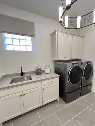 A modern laundry room with sleek gray appliances, ample cabinetry, and stylish lighting.