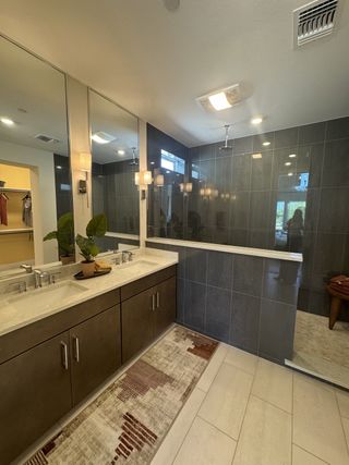 A contemporary bathroom featuring dual sinks, large mirrors, and a sleek glass shower with dark tile accents.