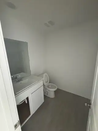 A simple bathroom featuring a pedestal sink, large mirror, and tile flooring.