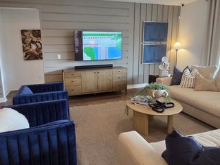 A modern living room with plush blue chairs, a wooden media console, and stylish decor on neutral furnishings.
