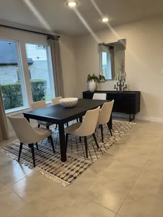 A modern dining area with a sleek dark table, cream chairs, decorative rug, and an elegant mirror over a black buffet.