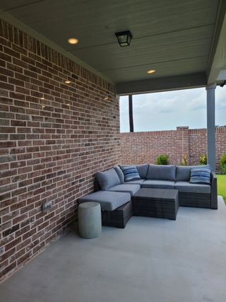 A cozy patio with a brick wall, gray sectional sofa, and a view of the green backyard, perfect for relaxation.