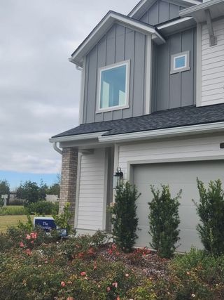 A modern two-story home with gray and white siding in Granville at eTown by David Weekley Homes (Jacksonville, FL) features a garage and landscaped garden.