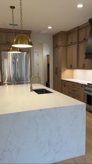 Model Home Kitchen: A sophisticated kitchen with a waterfall quartz island, warm wood cabinetry, and brass pendant lighting for a modern touch.