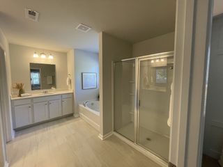 Spacious bathroom with dual vanity, glass shower, and a bathtub, featuring soft lighting and modern decor.