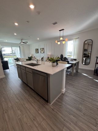 A modern kitchen with sleek gray cabinets, open plan living area, wood flooring, and elegant lighting.