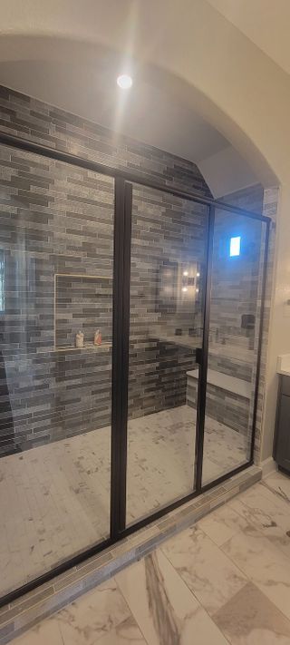 A sleek bathroom with a spacious glass shower, featuring dark tile walls and a marble floor for a luxurious feel.