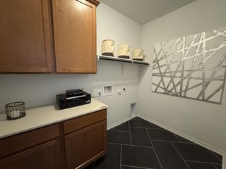 A modern laundry room with sleek cabinets, geometric wall art, and a built-in shelf on dark tiled flooring.