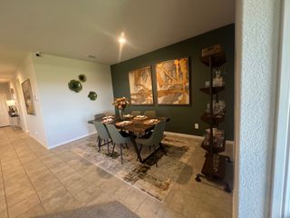 A modern dining area with artistic wall decor, a wooden table, and elegant green chairs, set on a tiled floor.