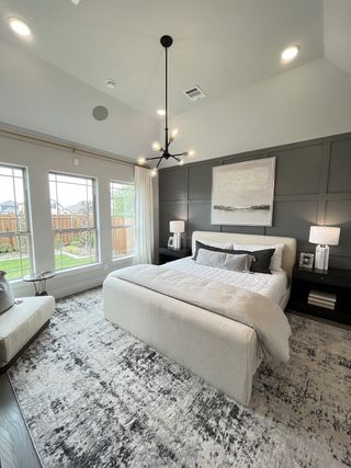 A modern bedroom featuring a cozy bed, elegant chandelier, and large windows overlooking a private garden.