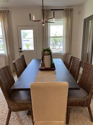 A cozy dining room featuring a dark wood table, wicker chairs, soft curtains, and a chic modern chandelier.