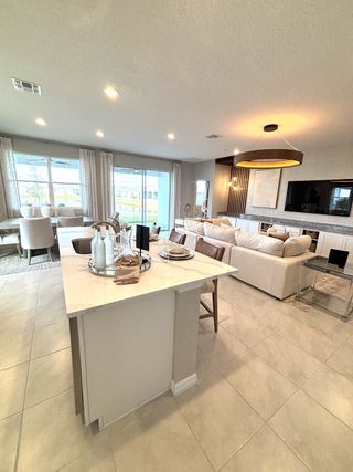 A modern open living area with elegant lighting, a large island, and cozy seating, perfect for entertaining guests.