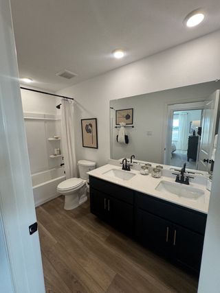 A modern bathroom with double sinks, wood flooring, black cabinetry, and elegant fixtures.