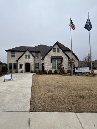 Grand stone-finished house with a large driveway, well-maintained landscaping, and Bloomfield Homes signage.