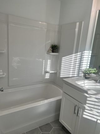 A bright bathroom featuring a sleek white bathtub, modern vanity, and hexagonal floor tiles.